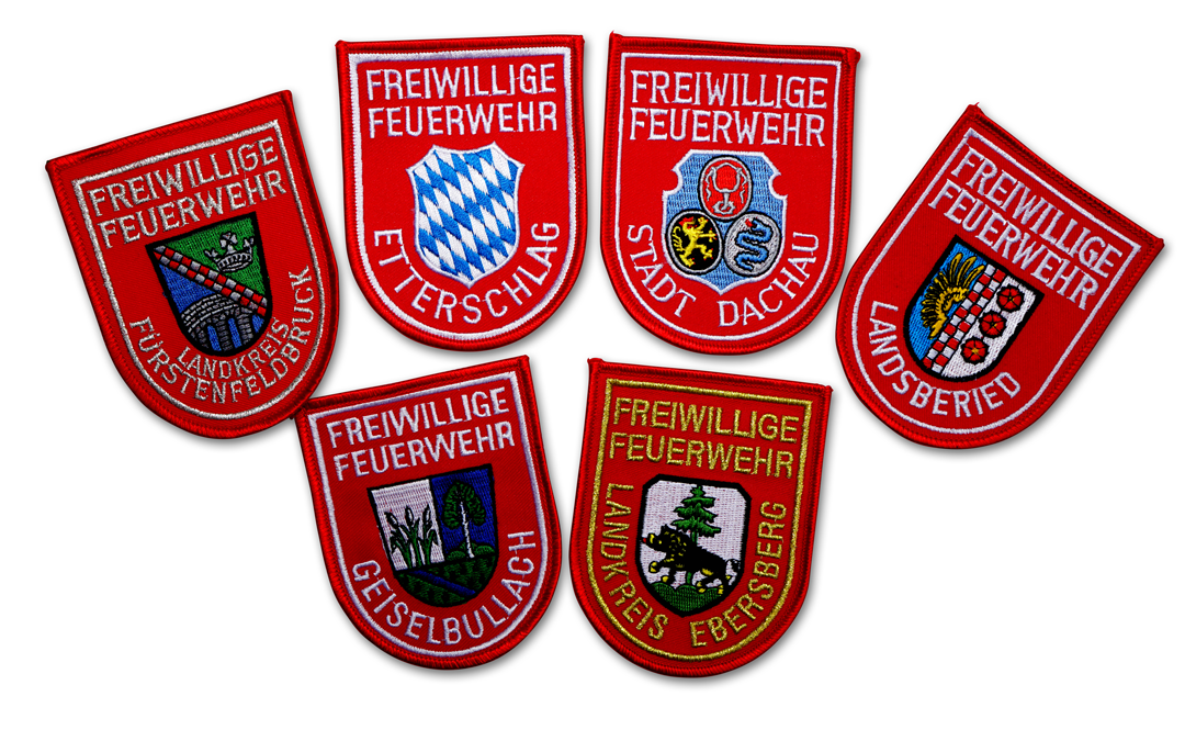 Fein gesticktes Armabzeichen mit weißer Schrift auf rotem Grund. Mit Text Freiwillige Feuerwehr und dem jeweiligen Ortsnamen. In der Mitte ist die Abbildung des Ortswappens oder ein Rautenwappen, je nach Wunsch