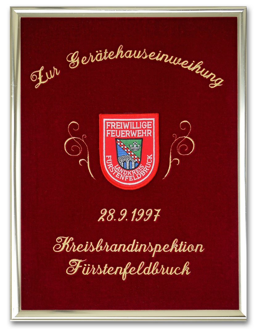 Gestickte Ehrentafel zur Gerätehauseinweihung. Schrift in Glanzgold gestickt. Als Motiv ist ein original Feuerwehr-Ärmelabzeichen aufgenäht.